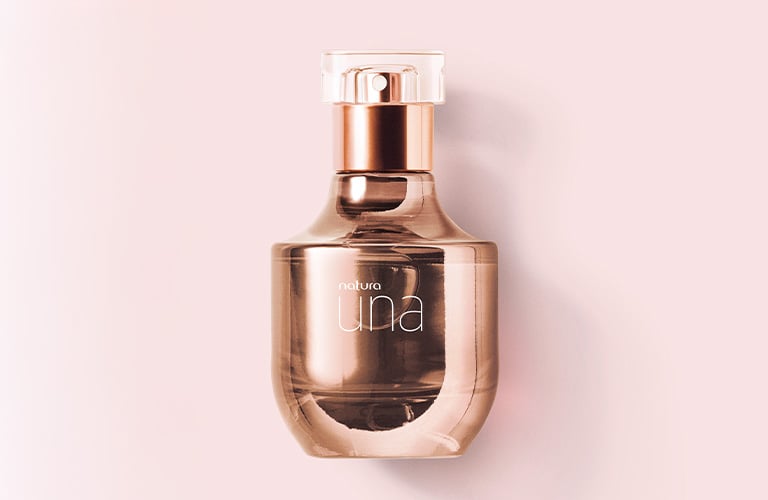 Fotografía de un frasco de perfume Luna en tono dorado rosado. El fondo es de color rosa claro, resaltando el diseño elegante y curvo del frasco.